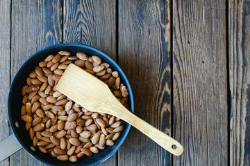 roast raw almond in pan with wooden spatula and wooden background