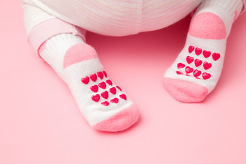 Baby crawling on light pastel pink floor. Feet in anti slip socks with heart shapes. Pastel color. Closeup. Back view.