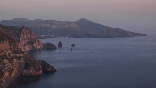 Time lapse of Italian island Lipari coast with island Vulcano in the distance during sunset, boats moving in the sea, sun on cliffs, Aeolian Islands Sicily
