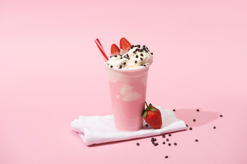 Disposable cup of milkshake with drinking straw, chocolate chips and strawberries on napkins on...