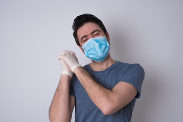 Dreamy young male with pleasant expression, closes eyes, keeps hands crossed near face, thinks about something pleasant, poses against gray background.