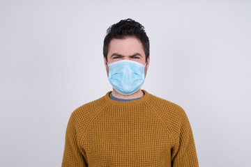 Mad crazy man clenches teeth angrily, being annoyed with coming noise, dressed in fashionable clothes, isolated over gray background. Negative feeling concept.