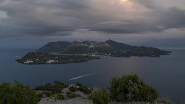Time lapse of Italian island Lipari coast in the foreground and with island Vulcano in the distance during sunset, boats moving in the sea, clouds in the sky, Liparic Islands Sicily
