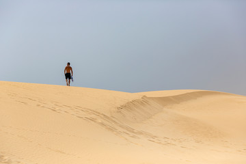 A young handsome man without shirt walking on the sand of the dunes in a beach of Fuerteventura