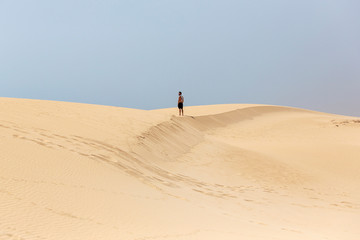 A young handsome man without shirt standing on the sand of the dunes in a beach of Fuerteventura