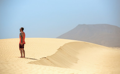 A handsome man looking at the horizon while standing on the sand dunes, in Fuerteventura, Canary islands, Spain