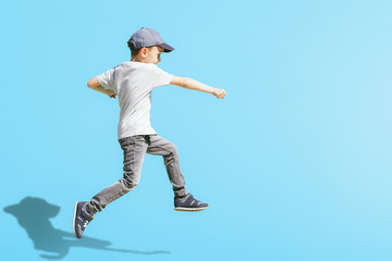 Young boy runs in the jump on the street on a bright blue background