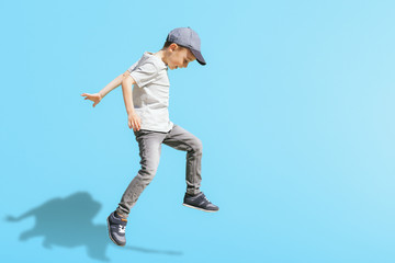 Fototapeta na wymiar Young boy runs in the jump on the street on a bright blue background