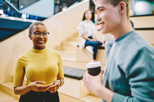 Cheerful African American And Japanese Friends 20 Years Old Enjoying Live Communication In University Campus, Prosperous Multicultural Hipster Guys Laughing During Coffee Break In Coworking Space