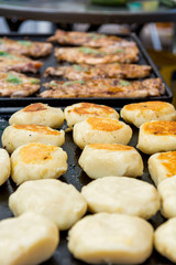 Delicious chicken steaks and fried bread buns on a grill.