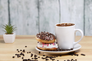 White coffee cup on a wooden table with chocolate and white chocolate donuts . Morning espresso. Morning cappuccino mug. 