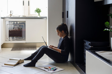 Adolescente coni capelli scuri raccolti e un maglia nera fa i compiti a casa seduta per terra