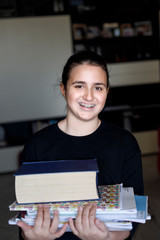 Fototapeta premium Ritratto di giovane agazza coni capelli scuri raccolti e un maglia nera che tiene in mano tanti libri per studiare, isolata su sfondo nero