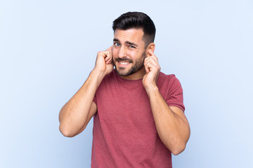 Young handsome man with beard over isolated blue background frustrated and covering ears