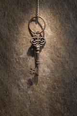old vintage door or chest key hanging on a chain against the background of a wall in a ray of...