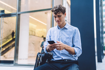 Handsome male professional trader using cellphone for checking financial information on website...