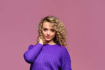 Obraz na płótnie Canvas beautiful young woman with curl hair in knitted violet sweater posing on pink background - Image