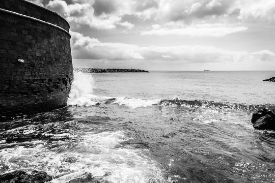 Wave splashing with violence by San Juan Bautista Castle wall in Tenerife. Atlantic ocean water from shore in Canary Islands. High contrast effect applied, black and white photography
