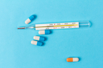 Pills isolated on blue background.Colorful medical drug capsule. Medical thermometer. Concept of coronavirus
