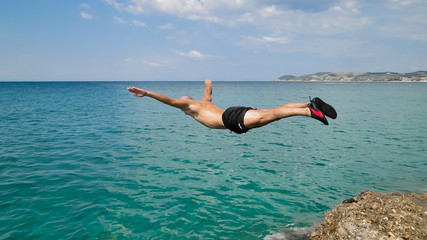 Mężczyzna skaczący do morza ze skał, uchwycony w locie.
