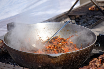 Pilaf prepare in a cauldron on a fire. Roasted carrots and meat. As a stage in the preparation of traditional pilaf.