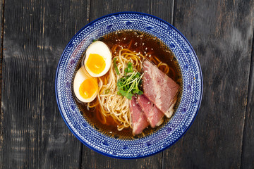 Top view on appetizing asian japanese shoyu ramen noodle soup with pickled agitama egg in a traditional blue bowl on the dark wooden table, horizontal