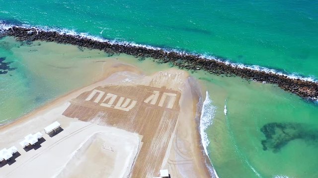 Happy Holiday in Hebrew letters written in Sand on a beach, Aerial view.