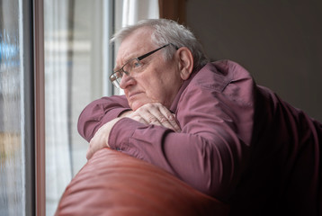 Bored man in sixties looking out the window in home 