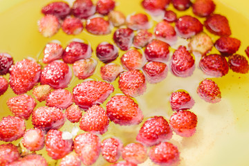 Little fresh berries of wild strawberry swim in groups in clear water in a yellow bucket. Selective focus.