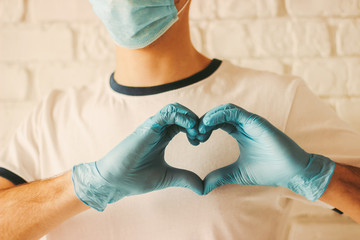 Young doctor in protective gloves and medical mask on face showing heart symbol. Man in medical...