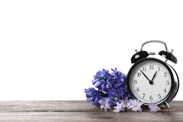 Black alarm clock and spring flowers on wooden table against white background, space for text. Time...