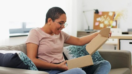 delivery, shipping and people concept - happy young african american woman opening parcel box with cosmetcis at home