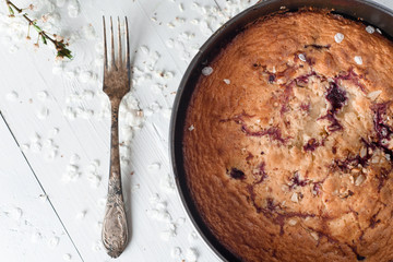 Cherry pie on a white wooden background. Nearby is an old silver spoon and spring flowering.