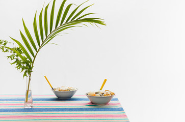 Obraz premium Healthy summer breakfast in the bowls on the table with colorful tablecloth and palm leaf. Vegan and vegetarian concept. Morning