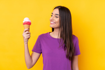 Young brunette woman with a cornet ice cream over isolated yellow background with happy expression