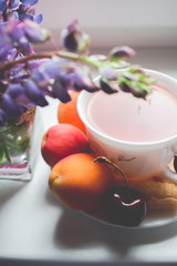 Tea time concept. Cup of tea with fruit and snacks and bouquet of flowers on window. Top view