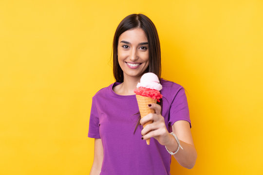 Young Brunette Woman With A Cornet Ice Cream Over Isolated Yellow Background With Happy Expression