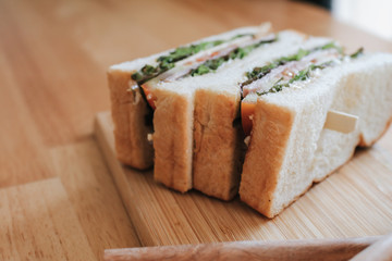 Homemade sandwich with ham, cheese, bacon, tomatoes, lettuce, cucumbers and onions on vintage wooden cutting board. with sunlight through window. Healthy alternative to burgers and grease.