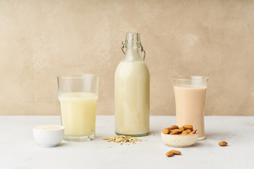Dairy alternative. Rice, oat and almond milk in bottles and glasses on beige background. Healthy protein vegan drink.