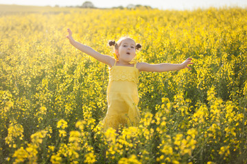 Cute girl in a yellow dress having fun in the field of flowering rape