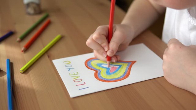 Girl drawing and coloring greeting card for Happy Mothers day with colorful pencils.