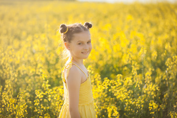 Fototapeta premium Cute girl in a yellow dress having fun in the field of flowering rape