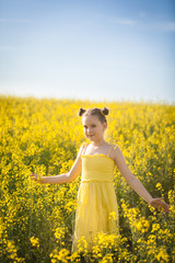 Naklejka na ściany i meble Cute girl in a yellow dress having fun in the field of flowering rape