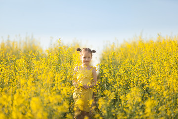 Cute girl in a yellow dress having fun in the field of flowering rape