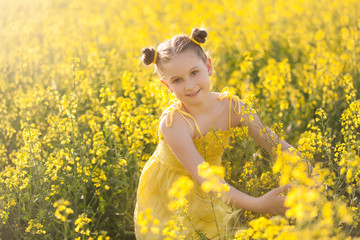 Naklejka na ściany i meble Cute girl in a yellow dress having fun in the field of flowering rape