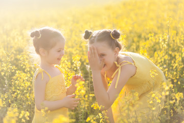 Cute girls in yellow dresses having fun in the field of flowering rape