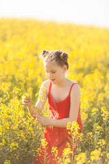 Naklejka na ściany i meble Cute girl in a red dress having fun in the field of flowering rape
