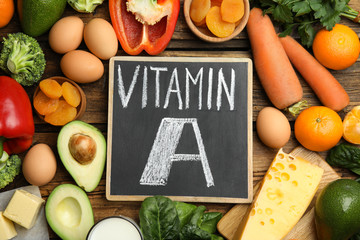 Chalkboard with phrase VITAMIN A and fresh products on wooden table, flat lay