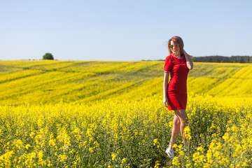 Happy young woman in a red dress in the rape field