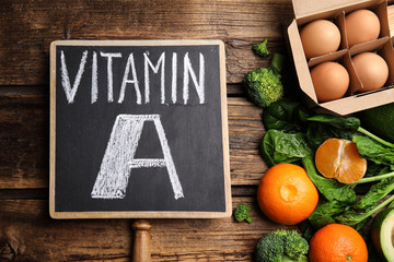 Chalkboard with phrase VITAMIN A and fresh products on wooden table, flat lay